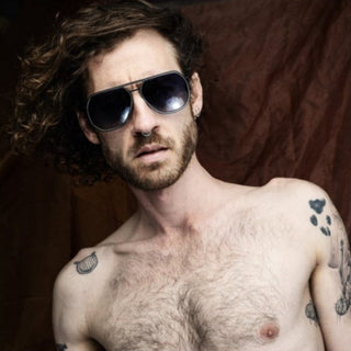 Man with tattoos wearing sunglasses against a dark background