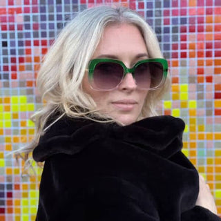 Person wearing green sunglasses and a black coat against a colorful mosaic background