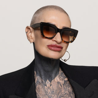 Person wearing black and tortoise sunglasses with a neutral background