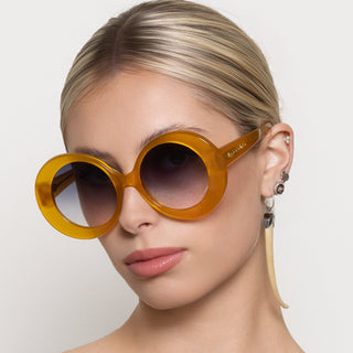 Woman wearing a pair of yellow round sunglasses with a neutral background