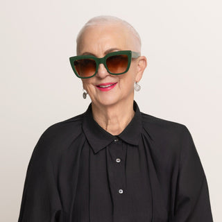 Woman wearing green sunglasses and a black shirt against a plain background