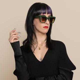 Woman wearing green sunglasses and a black outfit against a beige background
