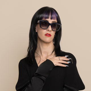 Woman wearing sunglasses and a black outfit against a beige background
