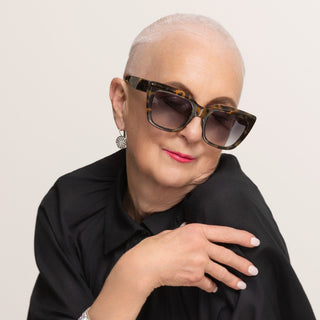 Woman wearing tortoiseshell sunglasses and a black outfit with a neutral background