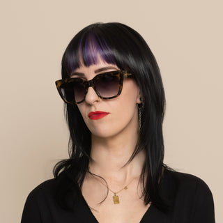 Woman wearing sunglasses and a black outfit against a beige background