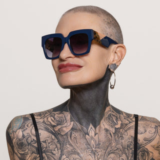 Person wearing a blue sunglasses with intricate tattoos