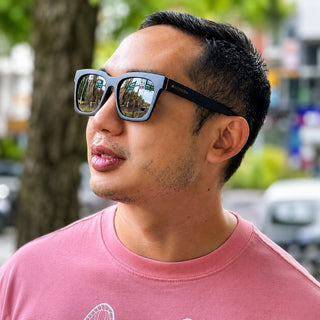 Man wearing sunglasses and a pink shirt outdoors with blurred background