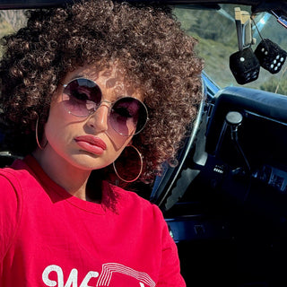woman with afro and round sunglasses sitting in car