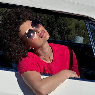 woman looking out of car with afro and round sunglasses