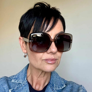 Person wearing large sunglasses and a denim jacket against a plain background