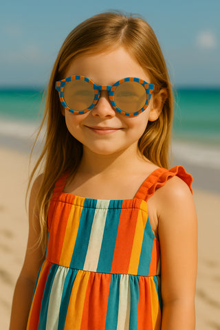 Young girl wearing colorful sunglasses and a striped dress on a beach