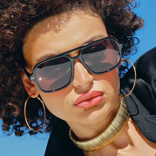 Woman wearing sunglasses and gold hoop earrings against a blue sky