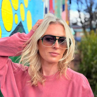 Woman wearing sunglasses and a pink sweatshirt in front of a colorful mural.