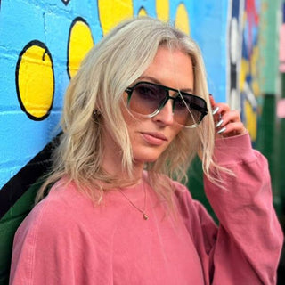 Person wearing double bridge sunglasses and a pink sweatshirt in front of a colorful mural