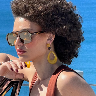 Woman with sunglasses and yellow earrings against a blue background