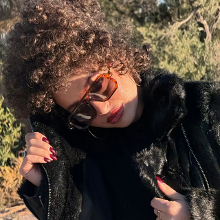 Person wearing sunglasses and a black coat with fur trim outdoors