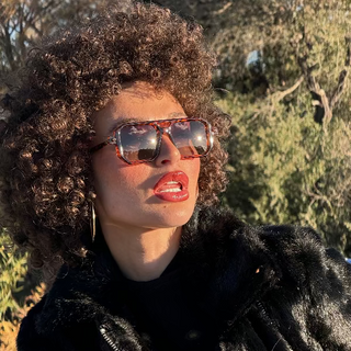 Person wearing sunglasses and a black fur coat outdoors