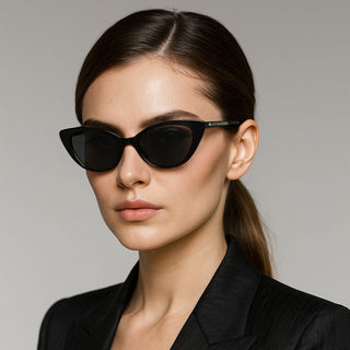 Woman wearing black cat eye sunglasses and a black outfit against a gray background