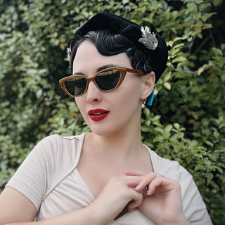 Woman wearing cat eye sunglasses and a vintage outfit with a green leafy background