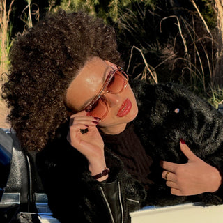 Person with sunglasses and a black jacket, surrounded by greenery.