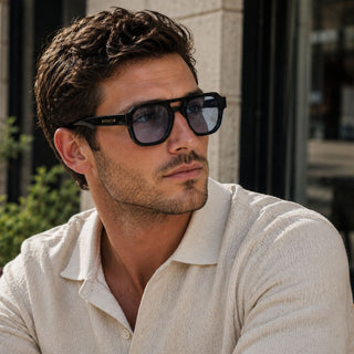 Man wearing sunglasses with blue lenses and a light-colored shirt outdoors
