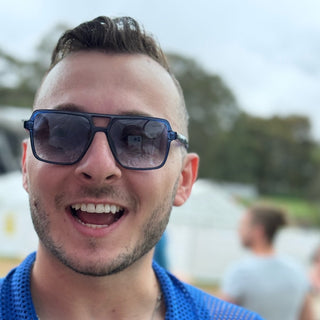 Man wearing sunglasses and a blue shirt with a blurred outdoor background