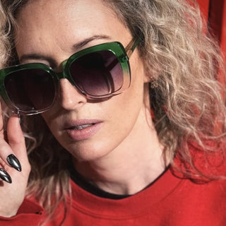 Woman wearing green sunglasses with a red background