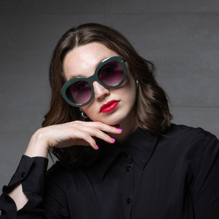 Woman wearing large sunglasses and a black shirt against a gray background
